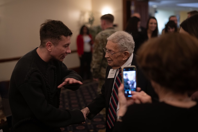 Two people shake hands as someone takes a photo.