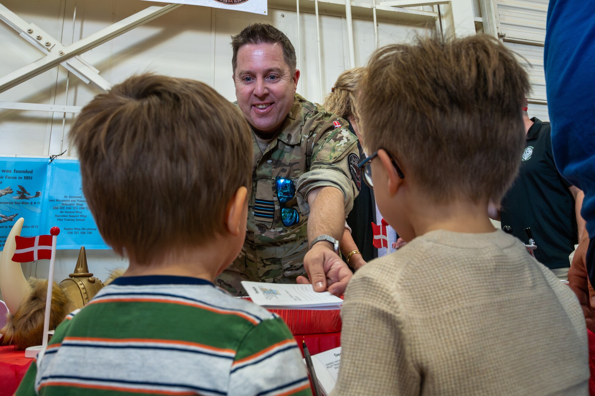 Danish Air Force Maj. Lars Kristensen, 308th Fighter Squadron participant maintenance liaison, stamps a fake passport for two children during the Luke Air Force Base International Festival 2024, Jan 26, 2024, at Luke AFB, Arizona.