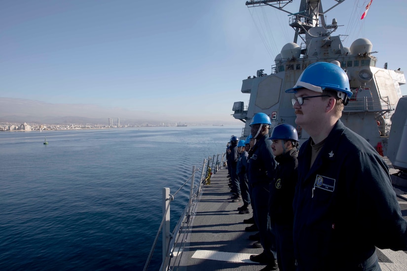 Sailors stand aboard a ship at sea.