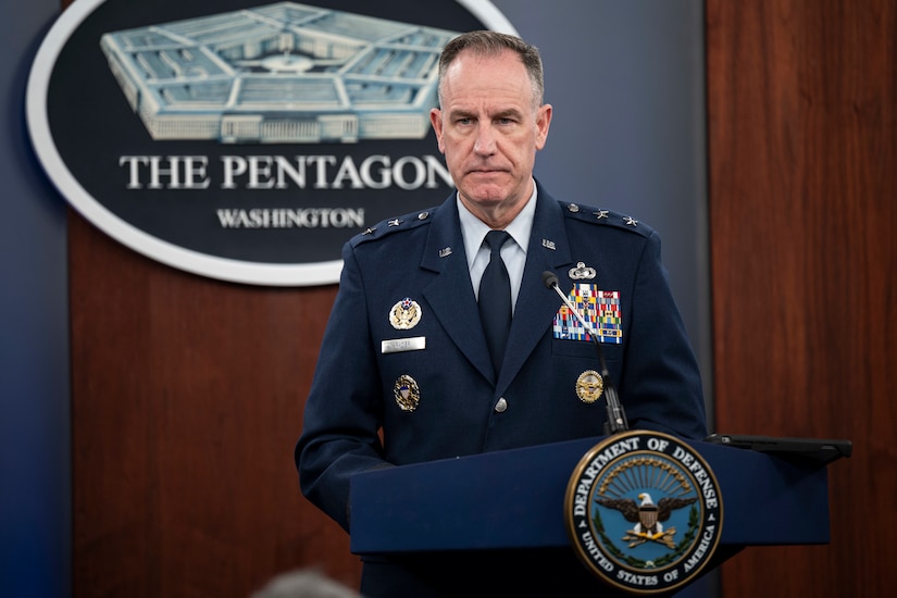 A man in a military uniform stands behind a lectern. The sign on the wall behind him indicates that he is at the Pentagon.