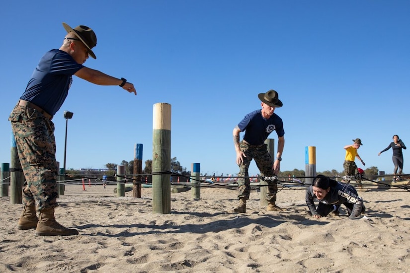 Three Marine drill instructors direct two women through an obstacal course.