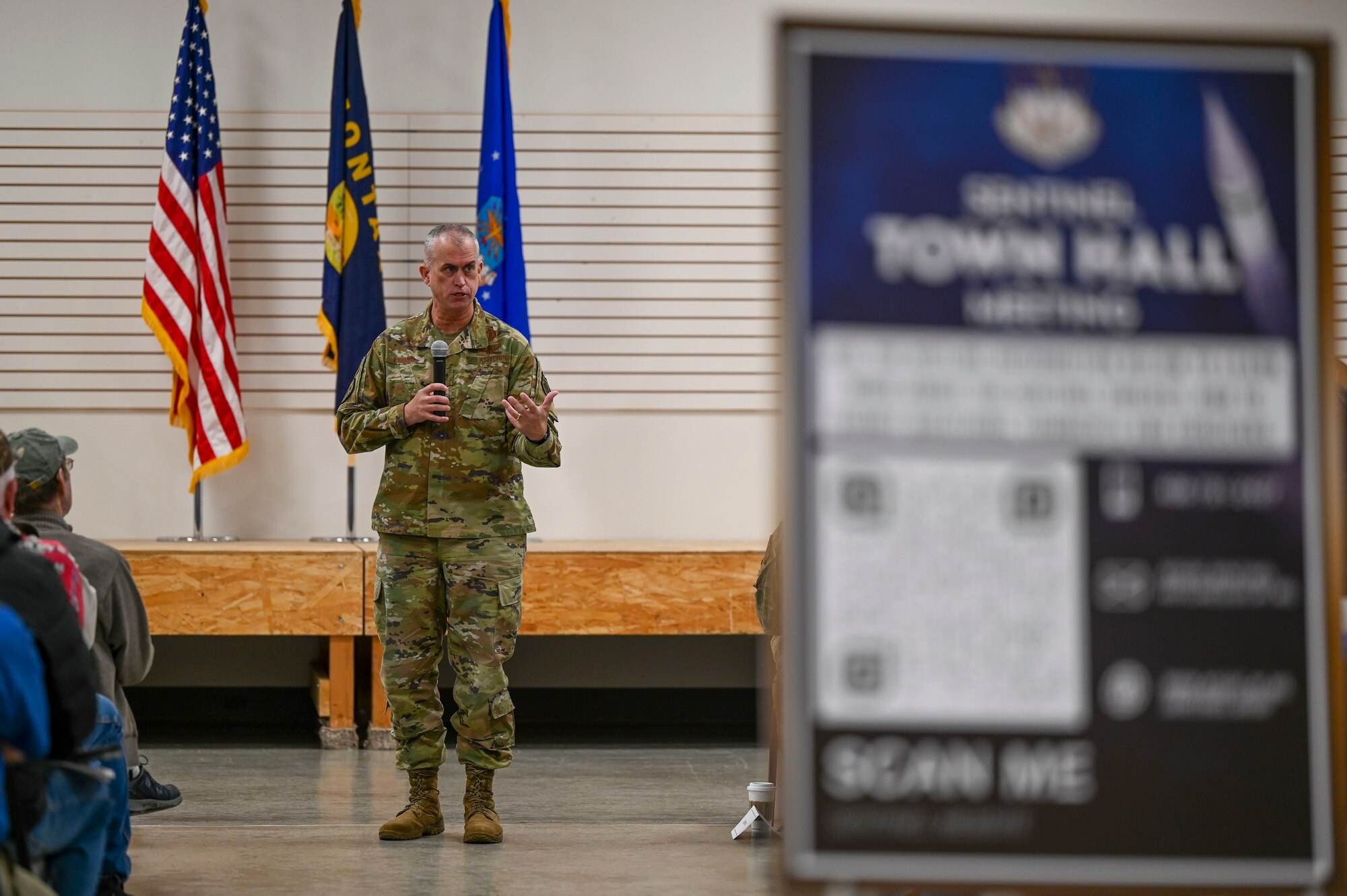A man speaks to an audience with a sign blurred out on the right of the photo.