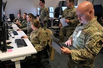 photo of uniformed military members working in a warehouse filled with computers and screens.