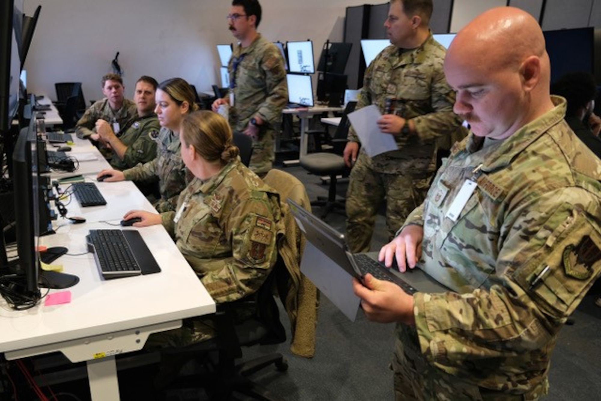 photo of uniformed military members working in a warehouse filled with computers and screens.