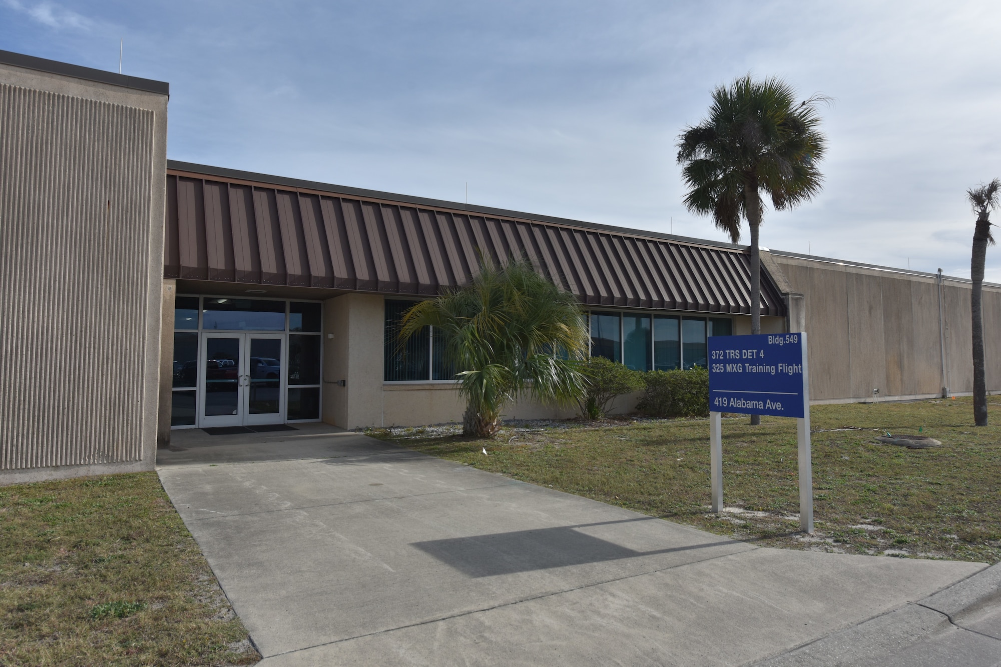 A building with a palm tree in front and a blue sign white text