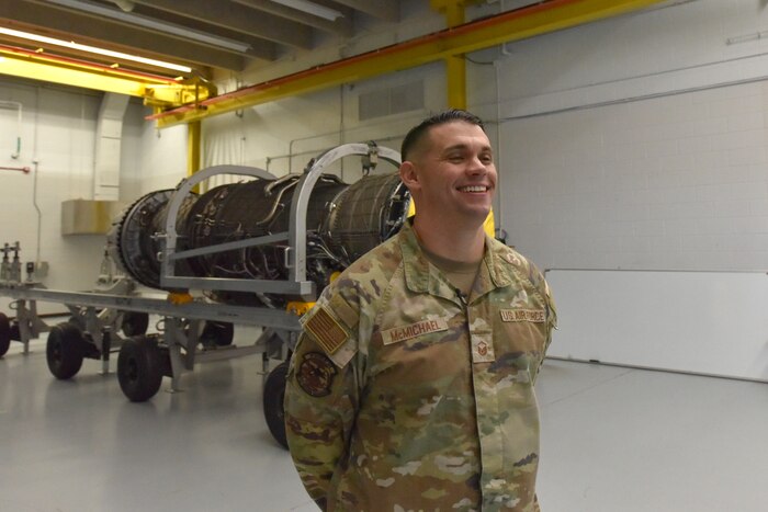 An Airman stands in front of a jet engine trainer