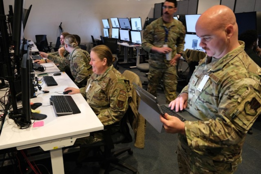 photo of uniformed military members working in a warehouse filled with computers and screens.
