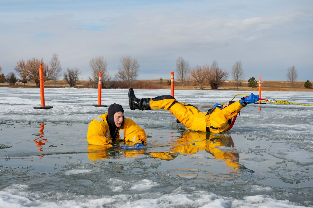 Two students in yellow cold weather gear participate in ice rescue training in a frozen lake.