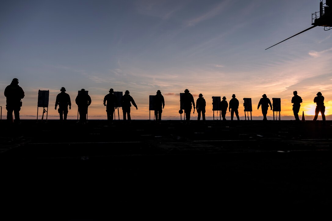 Sailors, shown in silhouette, check their shooting targets aboard a Navy ship.