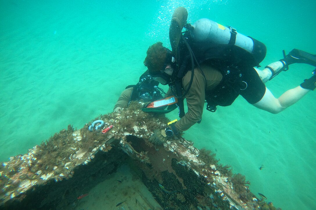 Two sailors attach lift bags to a submerged container during an underwater survey.