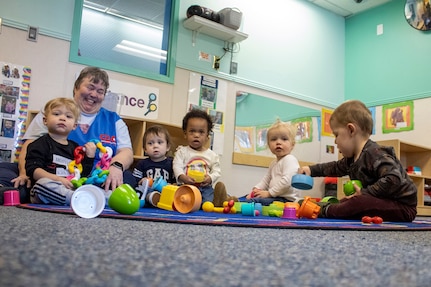 An adult smiles as children play with toys.