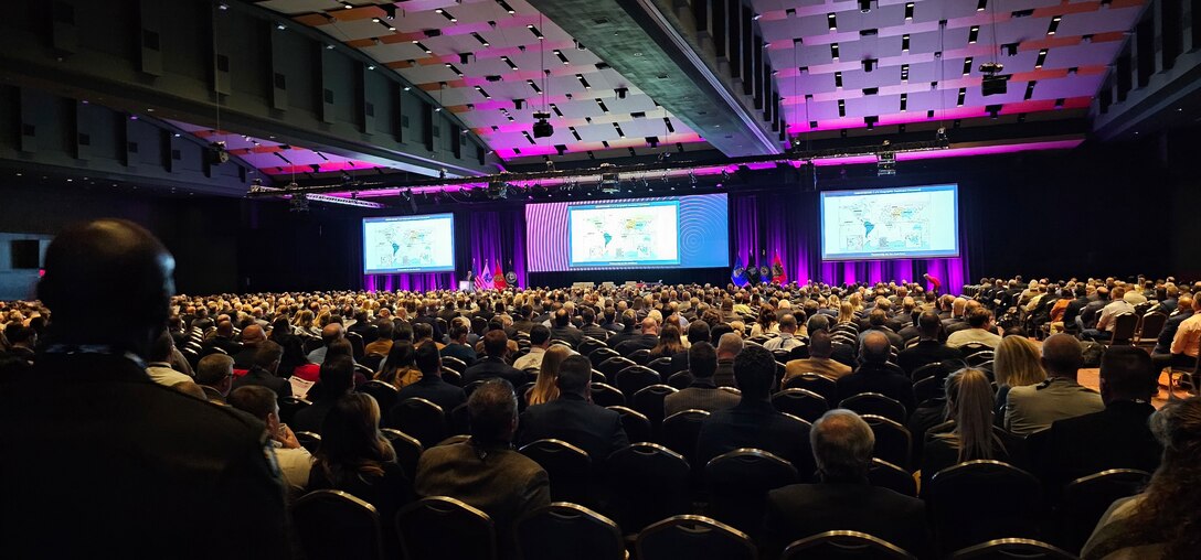 Groups of people from U.S. Army Corps of Engineers stand together to pose for a photo in business wear with booths surrounding them at the Small Business conference.