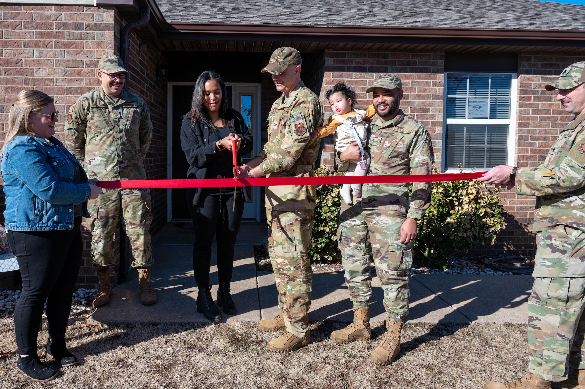 U.S. Air Force Col. Jeff Marshall, 97th Air Mobility Wing commander, and Roisveli Matos, Family Child Care (FCC) provider, cut a ribbon during a ceremony at Altus Air Force Base, Oklahoma, Jan. 29, 2024. The ceremony honored Matos’ accomplishment, officially opening her FCC home to provide care for families on base. (U.S. Air Force photo by Airman 1st Class Heidi Bucins)