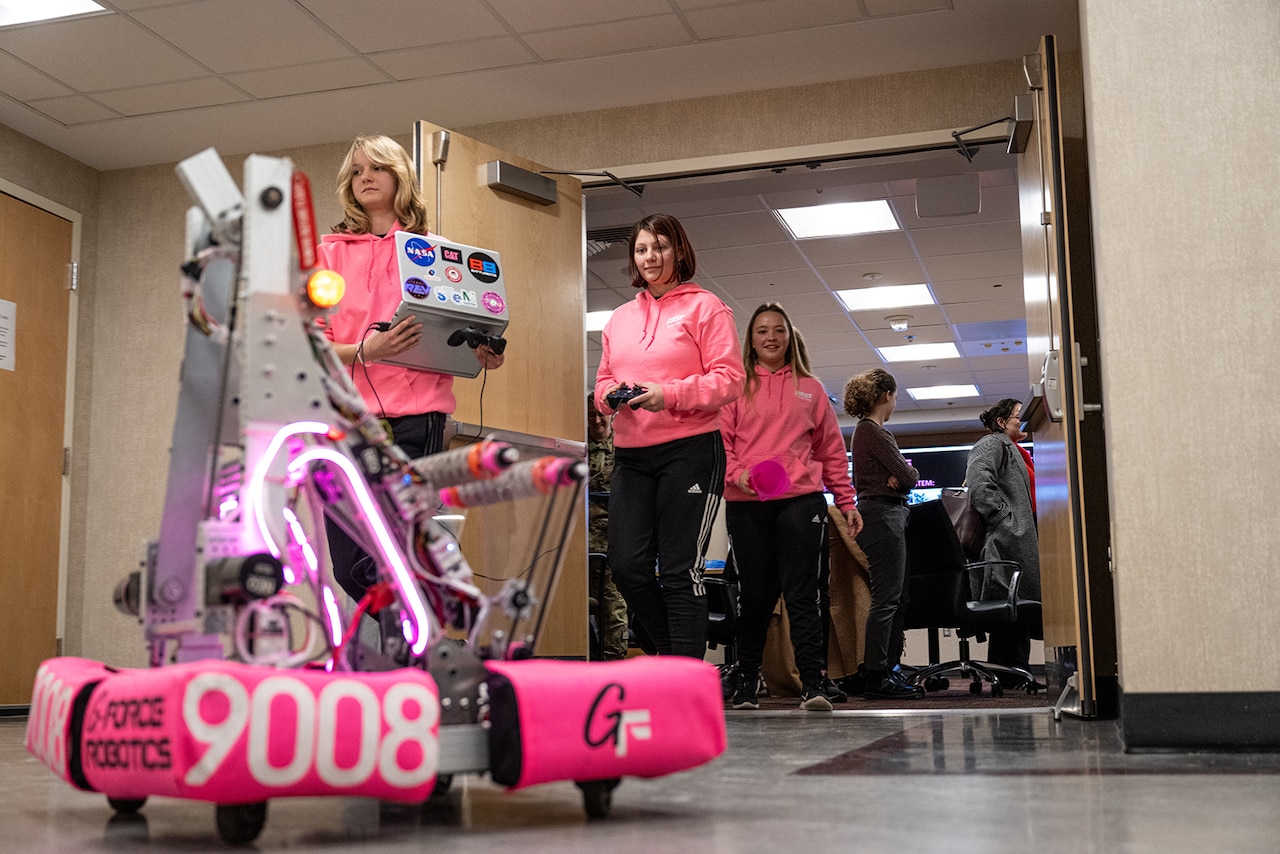 Two young people operate a robot while others stand in the background.