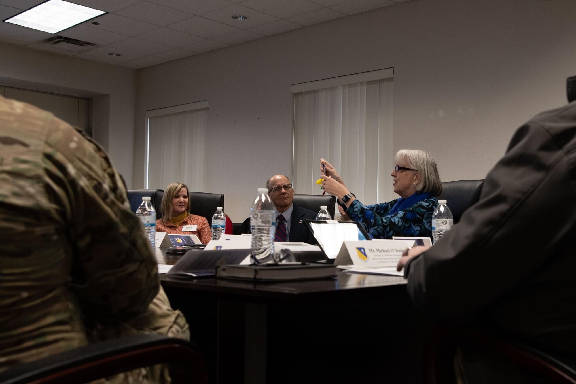 A woman talks to a group of men and women in a conference room, holding up a keychain.