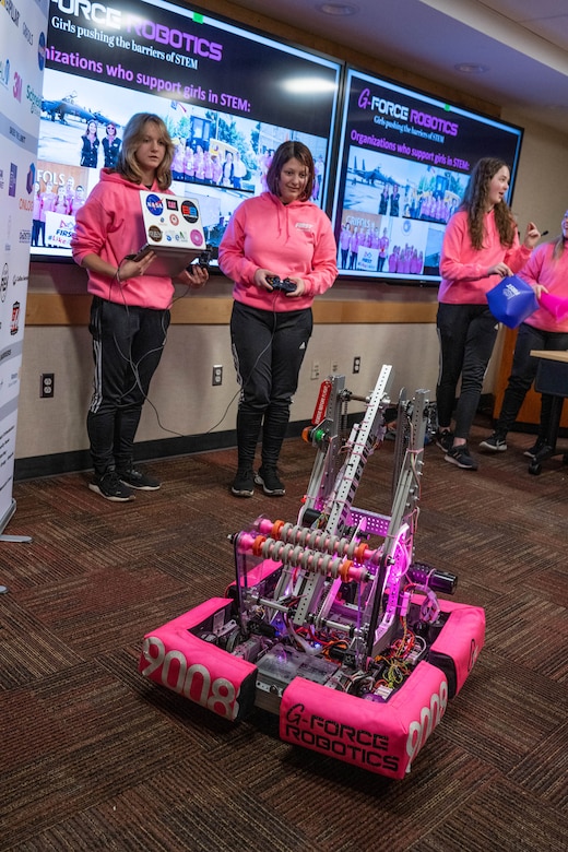 Two young people operate a robot while others stand in the background.
