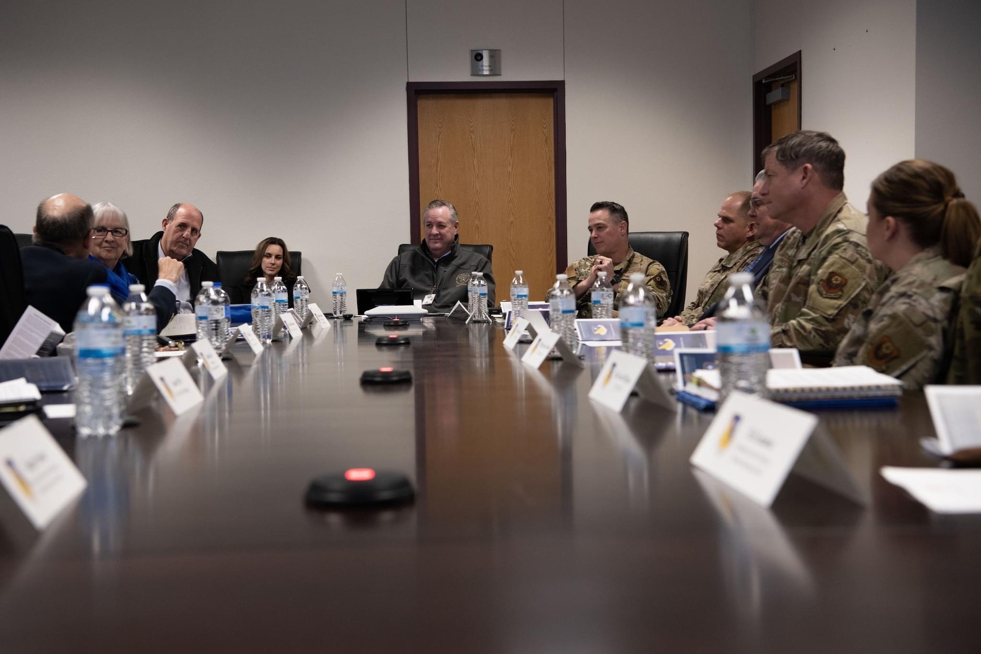 A group of men and women in business casual clothing sit at a conference table across from a group of women and women in uniform.