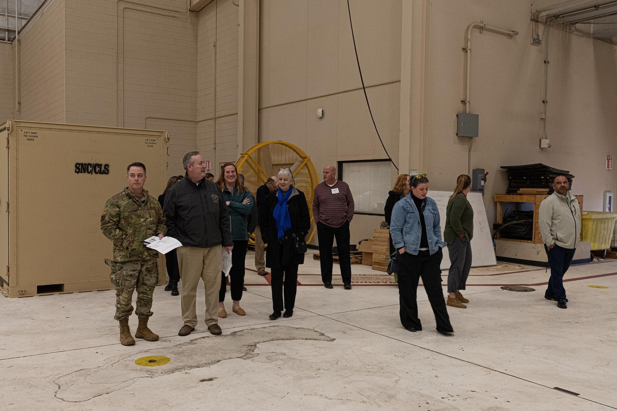 A group of men and women in civilian clothes walk in a building with one man in camouflaged uniform.