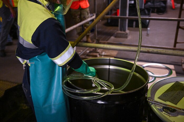 A member in support of Joint Task Force-Red Hill (JTF-RH) guides a drainage line into a fuel drum to remove residual fuel from the Red Hill Bulk Fuel Storage Facility Jan. 24, 2024, Halawa, Hawaii.