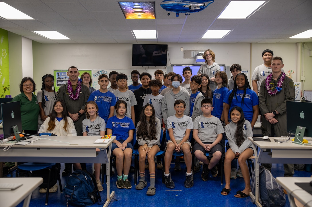 U.S. Marine Corps Cpl. Jacob Vasek and 1st Lt. Andrew Tilden with Marine Unmanned Aerial Vehicle Squadron (VMU) 3, Marine Aircraft Group 24, 1st Marine Aircraft Wing, pose for a group photo with students at Aliamanu Middle School, Hawaii, Jan. 26, 2024. Students learned about MQ-9A capabilities and aviation career fields in the Marine Corps. (U.S. Marine Corps photo by Lance Cpl. Logan Beeney)