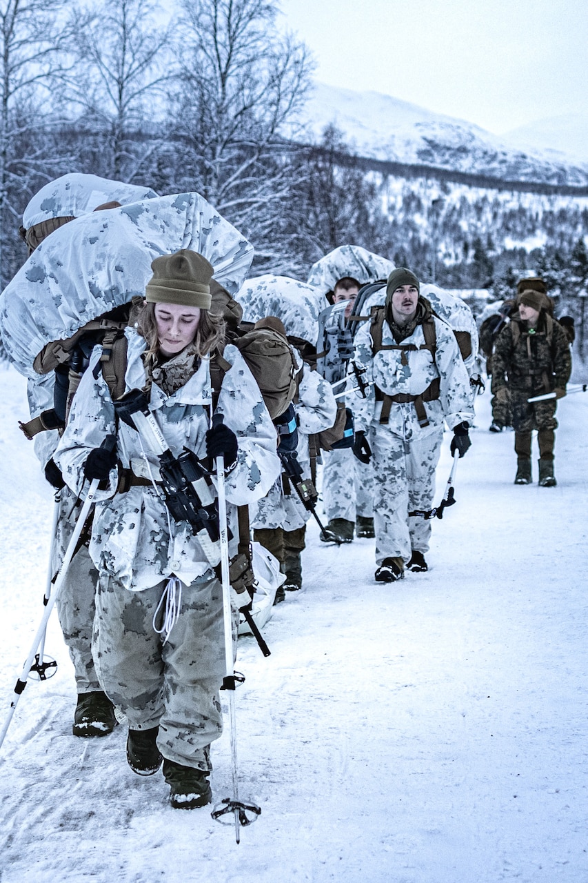 Marines and sailors hike in the snow.
