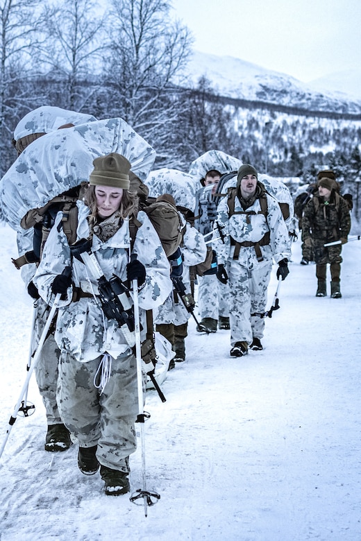 Marines and sailors hike in the snow.