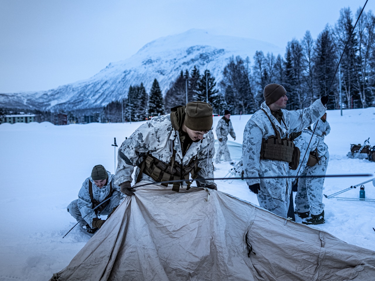 A Marine sets up a tent in the snow as fellow service members work in the background.