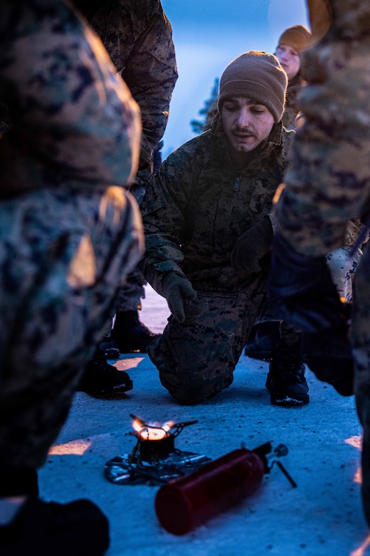 A Marine teaches fellow Marines how to use a portable stove in the snow.