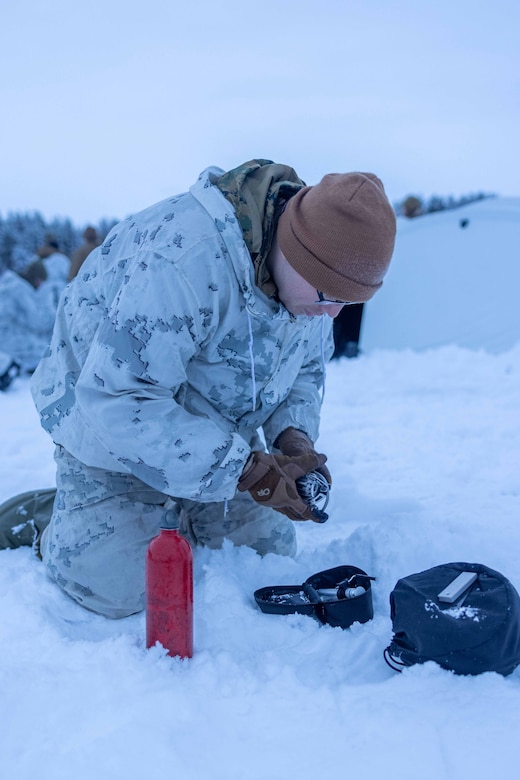 A sailor uses a portable stove in the snow.