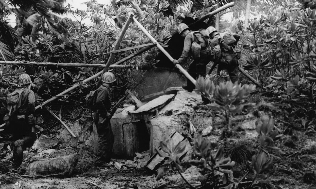 Infantrymen prepare to enter a well-camouflaged enemy bunker on Kwajalein with assistance from flamethrowers and demolitions teams.