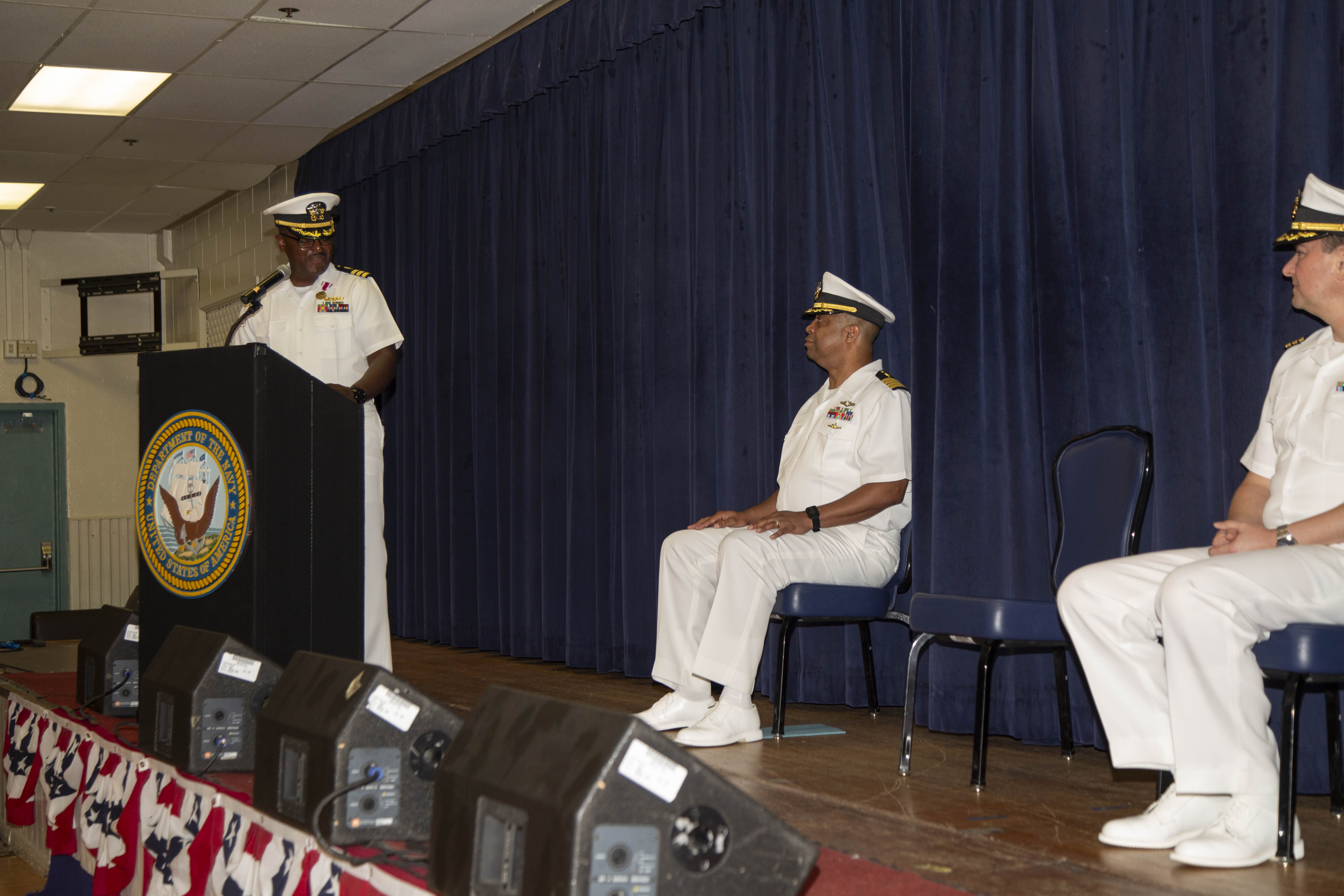 DIEGO GARCIA, British Indian Ocean Territory – Cmdr. Clifton Butler, outgoing officer in charge at Naval Medical Readiness Training Unit (NMRTU) Diego Garcia, speaks in front of Capt. Richard Gilliard, executive officer of U.S. Navy Medicine Readiness and Training Command Yokosuka Japan, and Cmdr. Kenneth Jenkins, incoming officer in charge for NMRTU Diego Garcia, during the NMRTU Diego Garcia change of charge ceremony onboard NSF Diego Garcia June 24, 2024. NSF Diego Garcia’s mission is to provide critical support to U.S. and allied forces forward deployed to the Indian Ocean, while supporting multi-theater forces operating in the CENTCOM, AFRICOM, EUCOM and PACOM areas of responsibilities in support of overseas contingency operations. (Courtesy photo by Nengh Dumlao)
