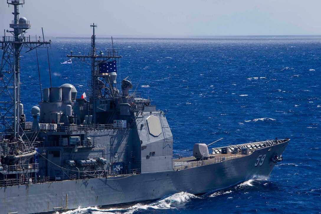 The front of a ship is visible in profile as it travels in blue waters.