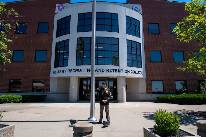 Man in Army uniform standing in front of building.