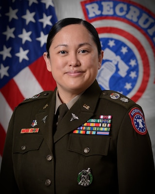 Woman wearing U.S. Army uniform standing in front of two flags.