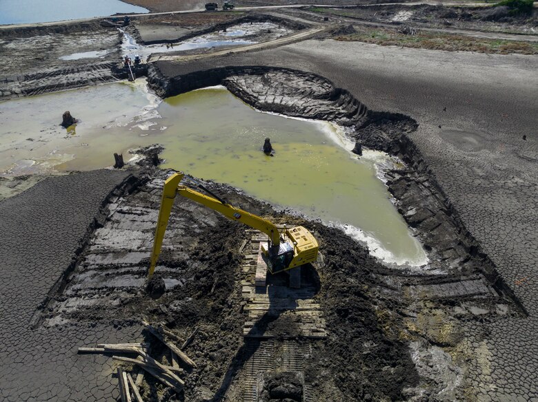A yellow piece of heavy equipment sits on black dirt with a green pool of water behind it.