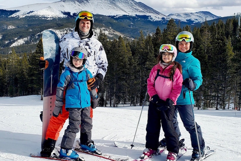 A family in ski gear poses for a picture on a mountain.