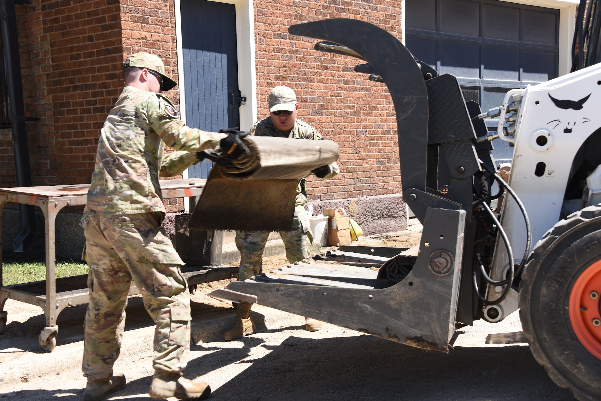 Senior Airman Brandon Stender, a 185th Air Refueling Wing Civil Engineering Squadron Water and Fuel Systems Maintenance specialist, left, and Senior Airman Nathan Gordon, a 185th Air Refueling Wing Emergency Manager, right, load debris into a skid steer loader bucket