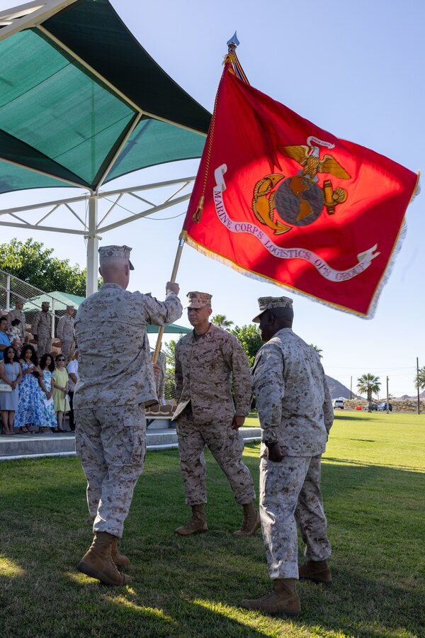 U.S. Marine Corps Col. Patrick Reynolds, a Bronx, New York native, outgoing commanding officer of Marine Corps Logistics and Operations Group, Marine Air-Ground Task Force Training Command, Marine Corps Air-Ground Combat Center, left, passes the colors to Col. Leonel Brito Jr., a Manhattan, New York native, incoming commanding officer of MCLOG, during a change of command ceremony at Lance Corporal Torrey Grey Field, MCAGCC, Twentynine Palms, California, June 21, 2024. The change of command ceremony represents the official passing of command from Reynolds to Brito. (U.S. Marine Corps photo by Lance Cpl. Anna Higman)
