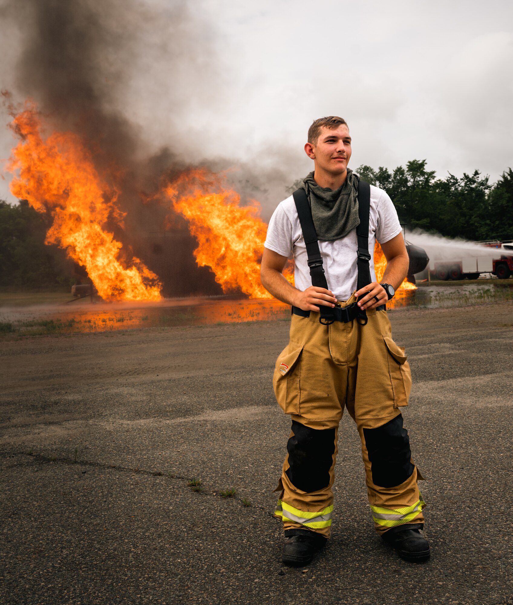An Airman poses for a photo with a fire exercise in the background