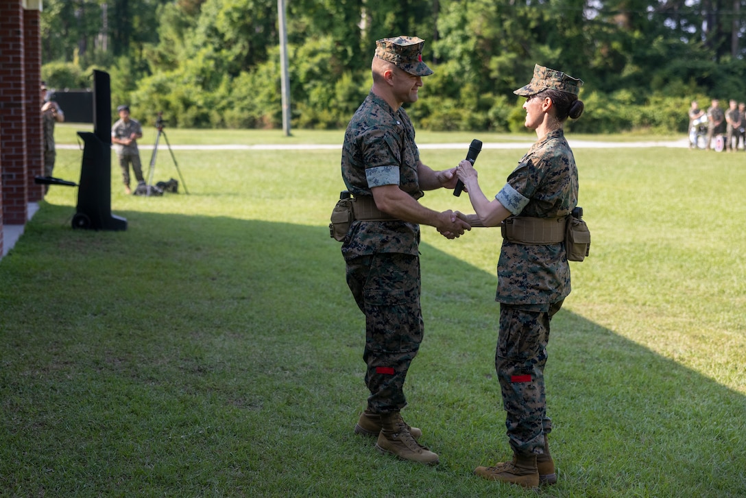 U.S. Marine Corps Lt. Col. Jon Peterson, left, commanding officer, 2nd Distribution Support Battalion, Combat Logistics Regiment 2, 2nd Marine Logistics Group, accepts a microphone from Lt. Col. Bethany Peterson, outgoing commanding officer of 2nd DSB, during a change of command ceremony on Camp Lejeune, North Carolina, June 27, 2024. During the ceremony, Lt. Col. Bethany Peterson relinquished command of 2nd DSB to her husband Lt. Col. Jon Peterson, after serving two years as the battalion’s commanding officer. (U.S. Marine Corps photo by Lance Cpl. Jessica J. Mazzamuto)