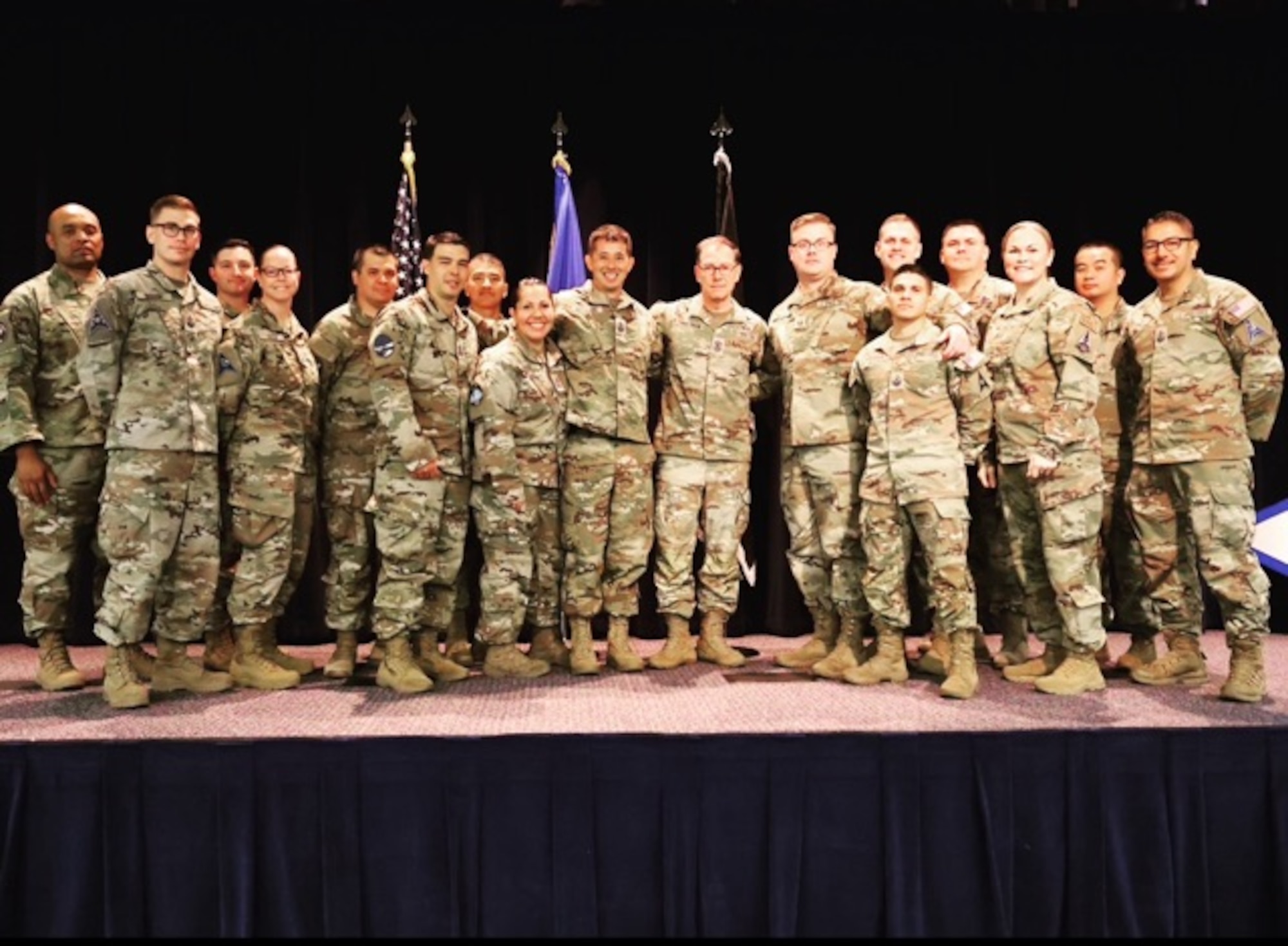 Individuals in uniform pose for a photo on stage.