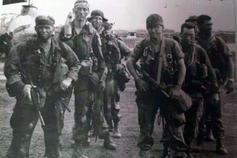 Eight service members in combat uniforms with rifles pose for a photo.