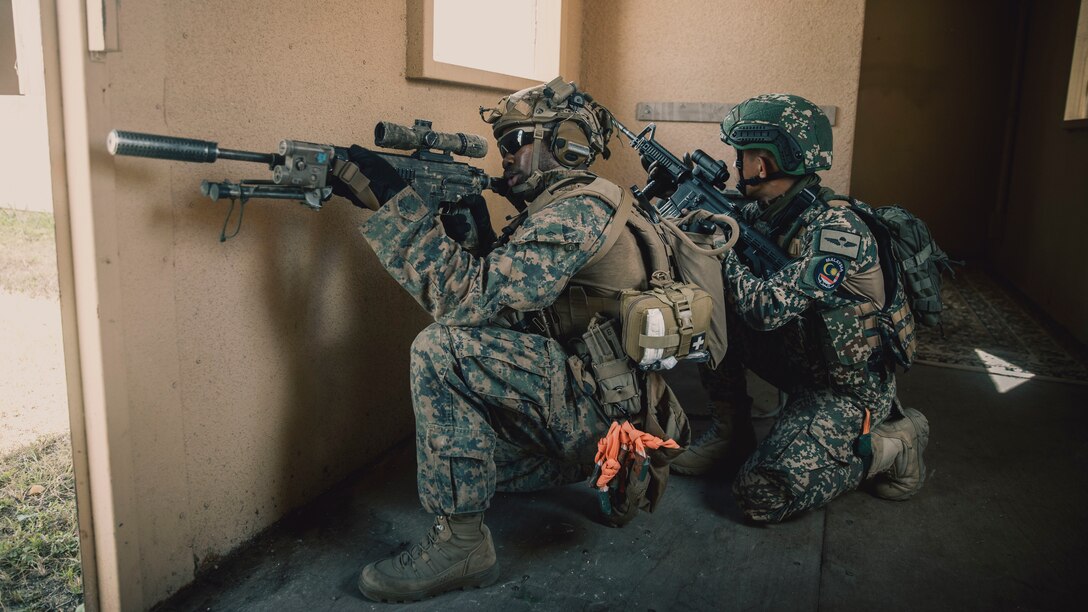 U.S. Marine Corps Lance Cpl. Dejanne Miller, a rifleman assigned to Battalion Landing Team 1/5, 15th Marine Expeditionary Unit, and a native of New York, and a Malaysian soldier assigned to 8th Battalion (Para), Royal Ranger Regiment, 10th Parachute Brigade, hold security inside the infantry immersion trainer at Marine Corps Training Area Bellows, Waimanalo, Hawaii, for Exercise Rim of the Pacific 2024, June 29, 2024. The IIT provided immersive scenario-based training to evaluate Marines and partner nations in infantry tactics. Twenty-nine nations, 40 surface ships, three submarines, 14 national land forces, more than 150 aircraft, and 25,000 personnel are participating in and around the Hawaiian Islands, June 27 to Aug. 1. The world’s largest international maritime exercise; RIMPAC provides a unique training opportunity while fostering and sustaining cooperative relationships among participants critical to ensuring the safety of sea lanes and security on the world’s oceans. RIMPAC 2024 is the 29th exercise in the series that began in 1971. (U.S. Marine Corps photo by Cpl. Joseph Helms)