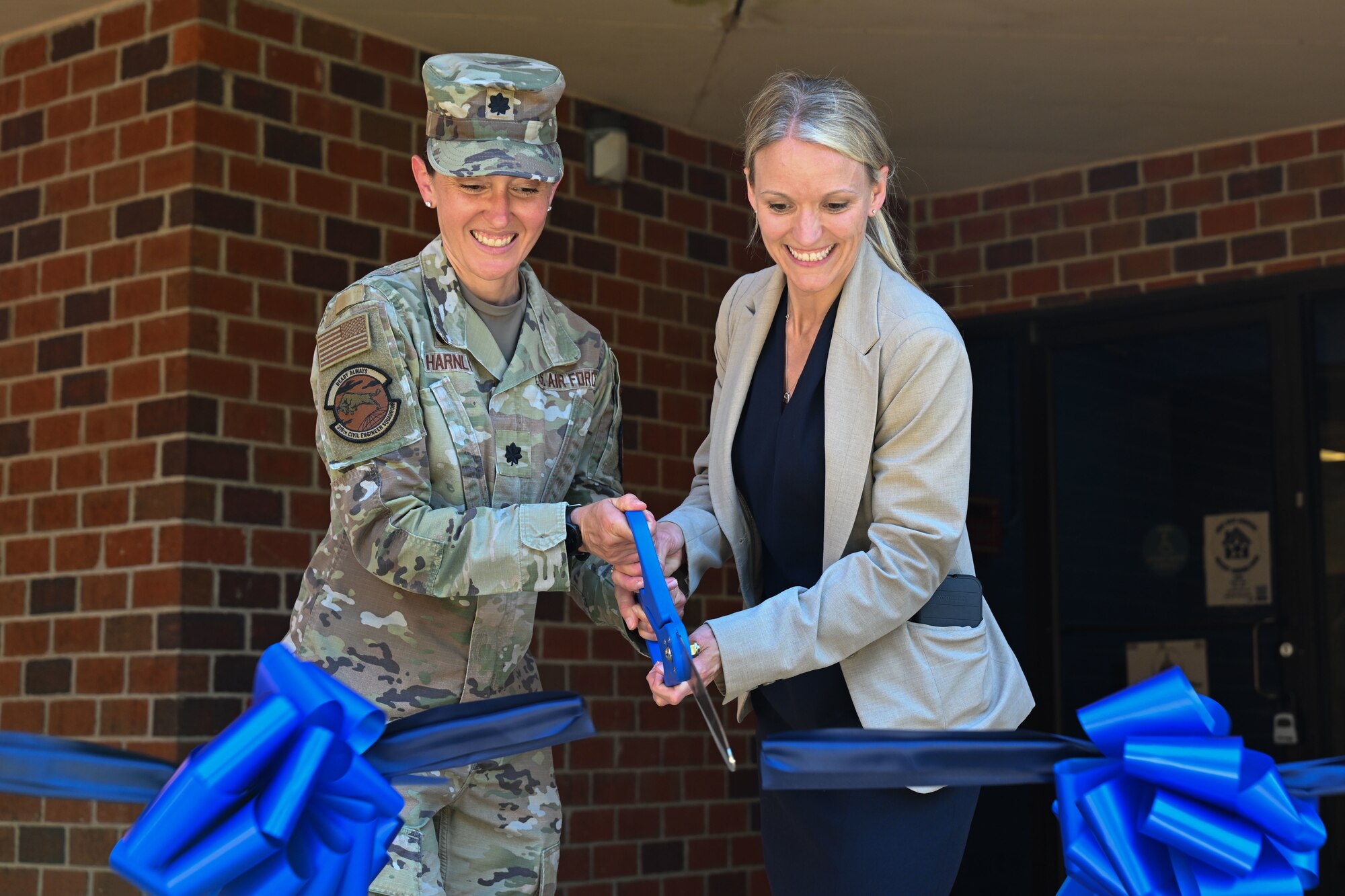 Two women holding a big pair of scissors, cutting a blue ribbon.