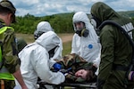 Members of the Colorado National Guard Chemical, Biological, Radiological and Nuclear Enhanced Response Force Package, joined by State Partnership Program partner the Republic of Slovenia, move a patient onto a stretcher for simulations during medical exercises Vigorous Warrior and Clean Care 2024 at Bakonykúti Training Area, Hungary, May 7, 2024. The CERFP, a domestic operations capability in the U.S., deployed to showcase the capability of doing mass decontamination in a battlefield setting while integrating emergent medical treatment. (U.S. Air National Guard photo by Airman 1st Class Eliana Raspet)