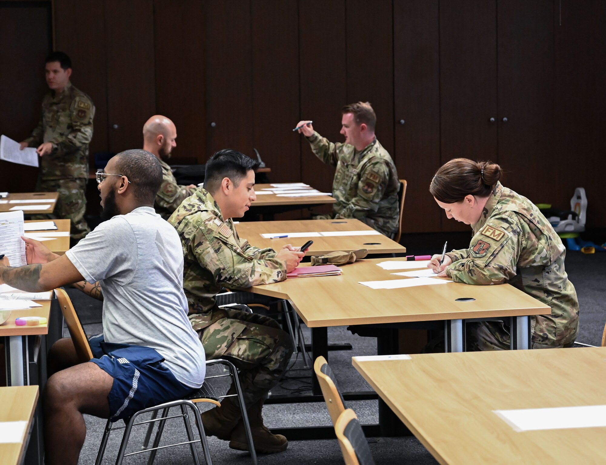 A group of Airmen sit at tables going over paper forms