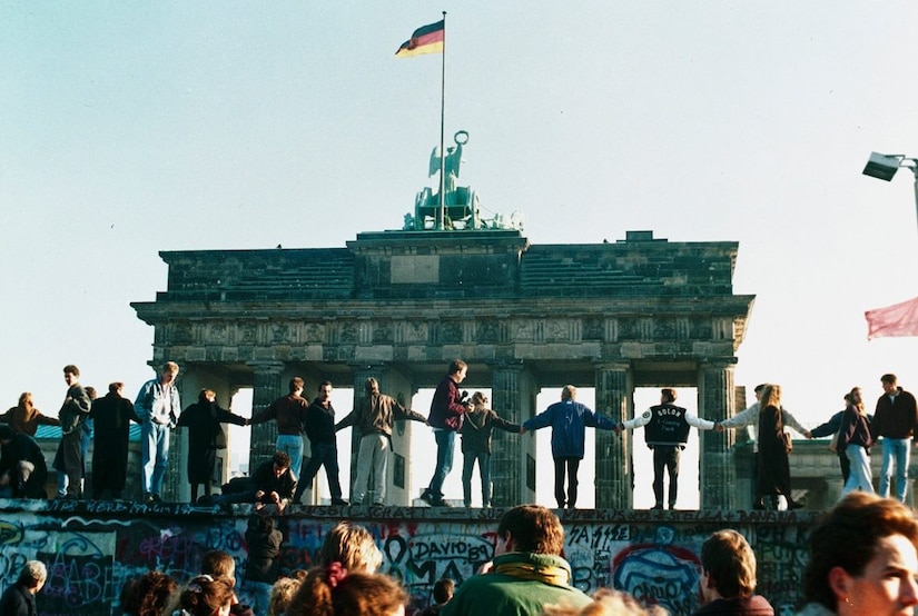 People holding hands stand on top of a wall as others look on.