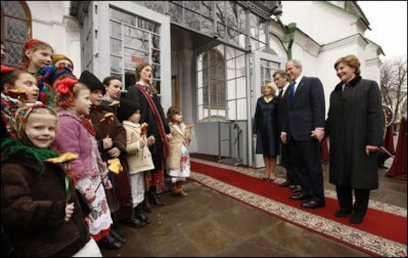 Four adults greet school children outside a church.