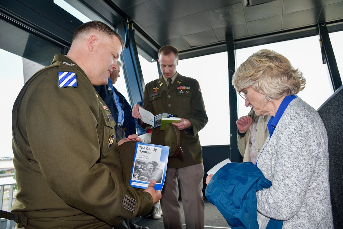 Denise Williams, daughter of the late Col. Gail Halvorsen, presents U.S. Army Corps of Engineers, Europe District Commander Col. Dan Kent with a gift of a commemorative coin and a book about her father with additional sections inspired by her father’s thoughts and teachings in the air traffic control tower on the Clay Kaserne portion of U.S. Army Garrison Wiesbaden June 15, 2024. They were there for a ceremony earlier in the afternoon dedicating and naming the new tower in honor of Halverson, who due to his actions during the Berlin Airlift earned the nickname the “Candy Bomber.” (U.S. Army photo by Chris Gardner)