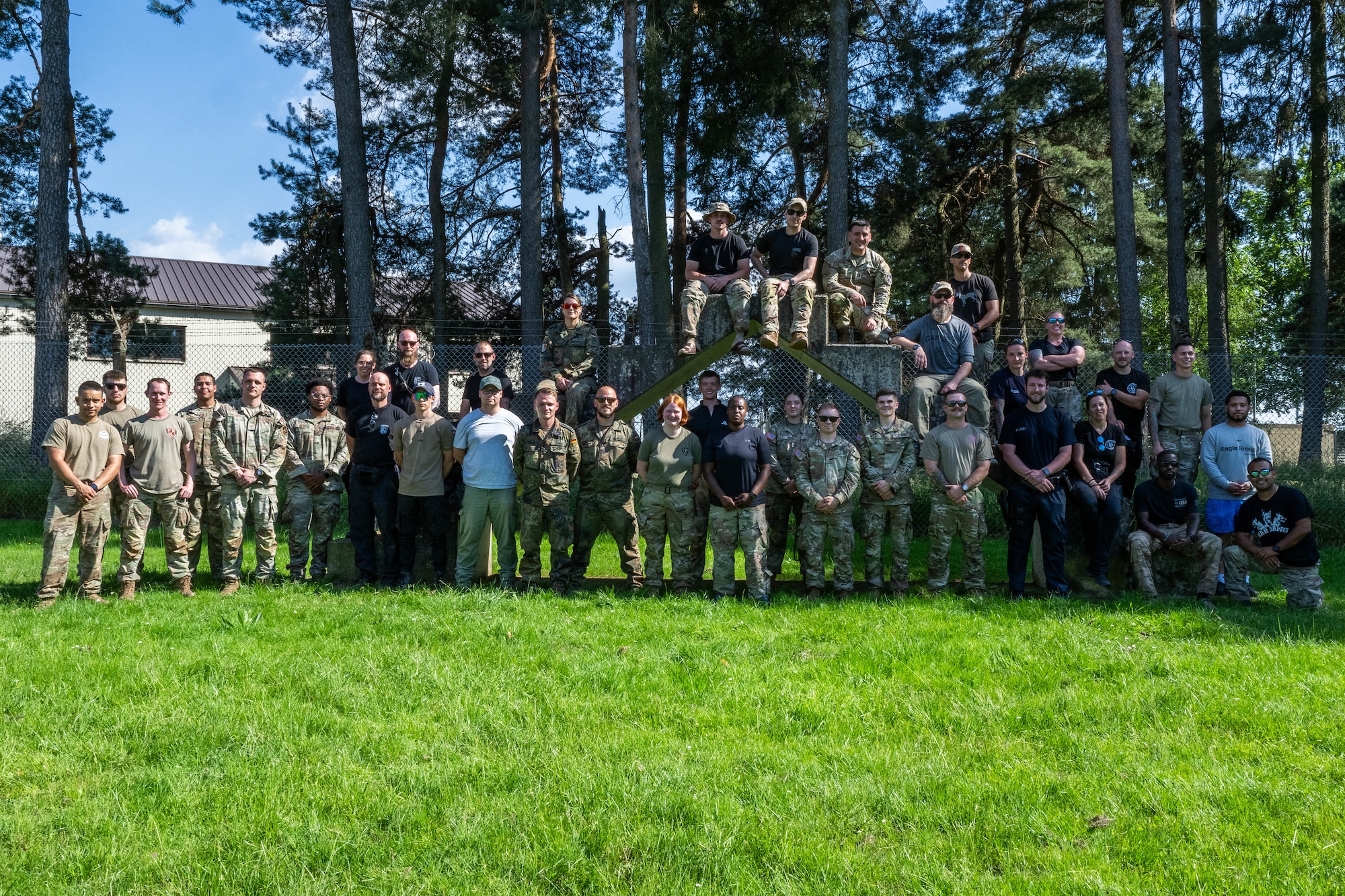 A group of soldiers, Airmen, and police officers gather in a grassy area for a photo.